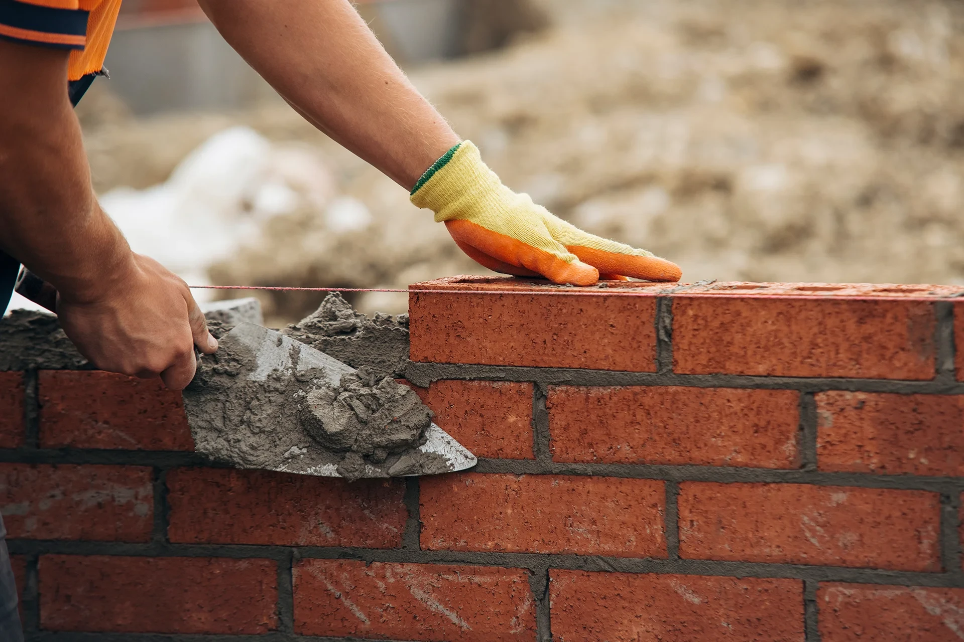 Chantier de construction extérieur avec homme en tenue de travail, casque de sécurité jaune, bras croisés devant bâtiments en construction